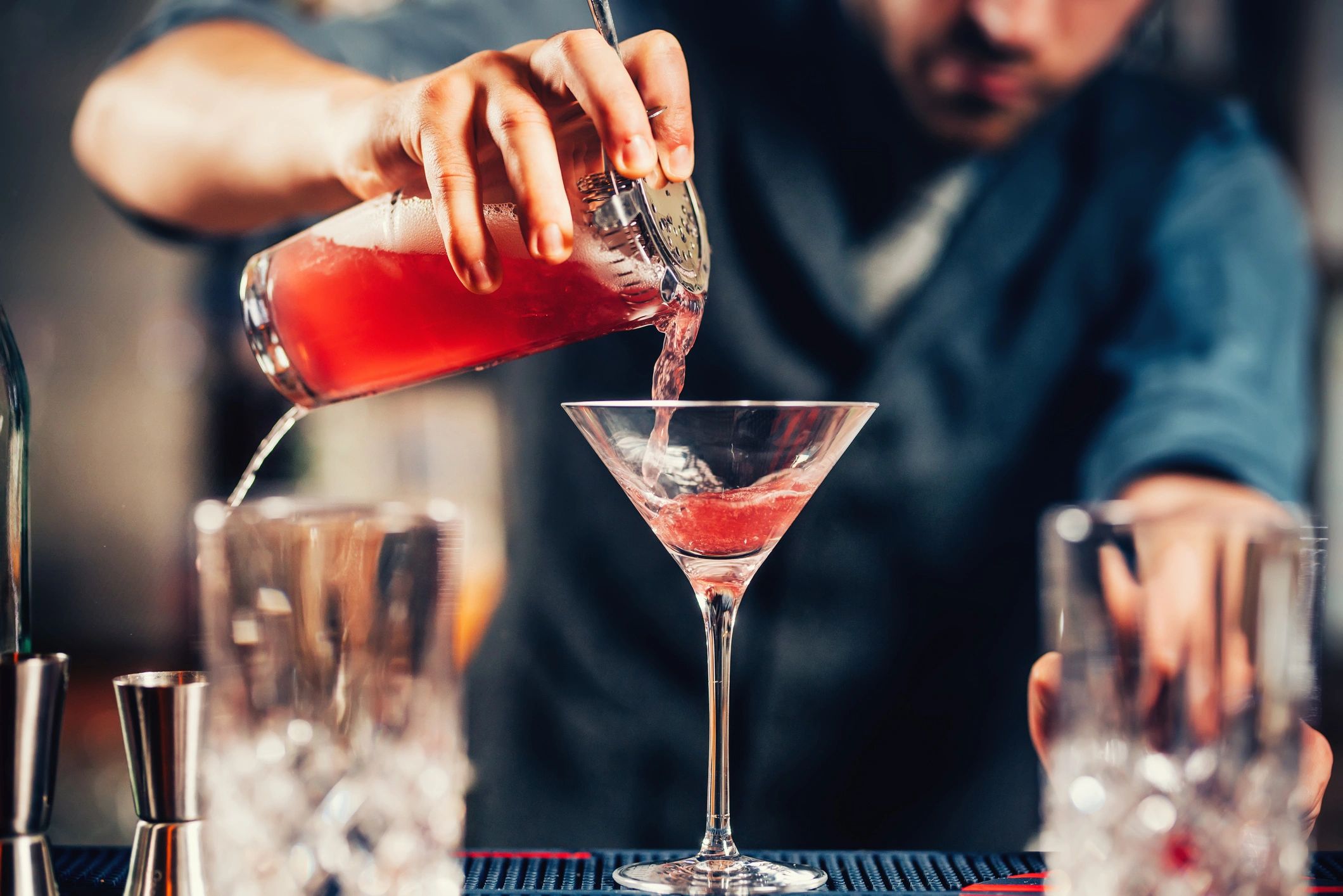 Bartender pouring a cosmopolitan cocktail into a martini glass